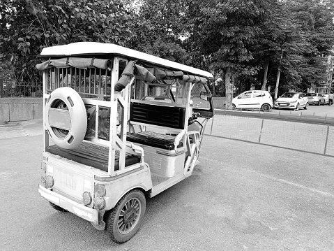 White electric rickshaw standing near barricade on road during day time outdoors.