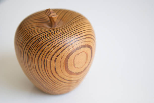 Apple carved out of grained wood sits with a light sheen on a white background