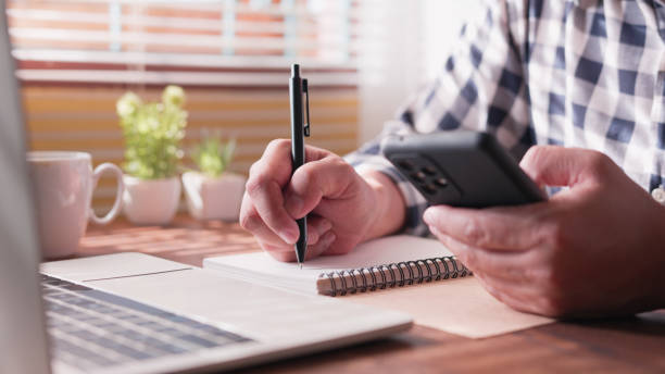 istock Hand a man typing keyboard laptop and writing with smartphone 1727873366