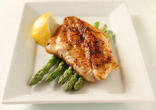 "Blackened catfish, pan fried flounder, or dover sole with paprika, red pepper flakes, asparagus and lemon.  Shallow dof, sharp focus on the asparagus tips and nearest 1/3 of the fish.  Not isolated, shot on white."
