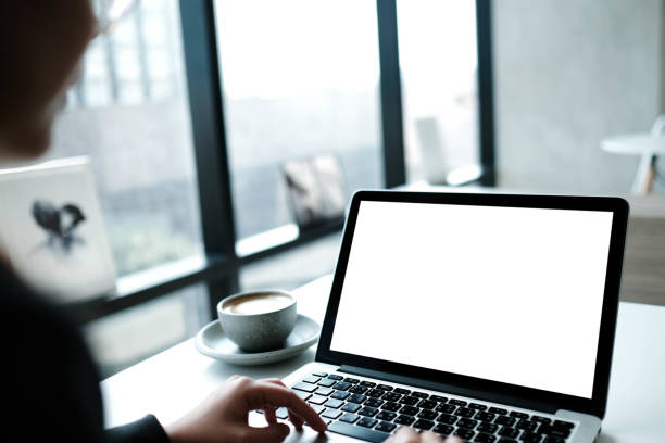 istock woman person sitting front open laptop with blank empty screen for your information or content while talking on smart phone in modern coffee shop. 1727876721