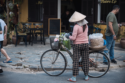 Hoi An – Cam Tanh, Vietnam - November 06, 2022: vietnamese woman with bicycle on street in ancient town Hoi An, Vietnam