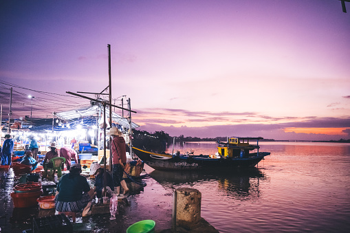 Hoi An – Cam Tanh, Vietnam - November 07, 2022: Vietnamese woman standing at pier of fish market in Hoi An at sunrise