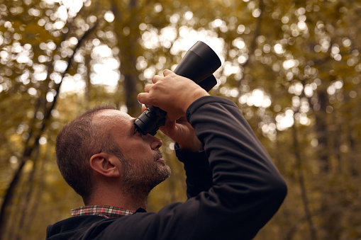 Man using binoculars for birdwatching and other observing animals in nature.