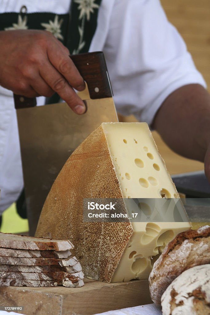 Slicing cheese A swiss man in a traditional costume is slicing a loaf of cheese. Cheese Stock Photo