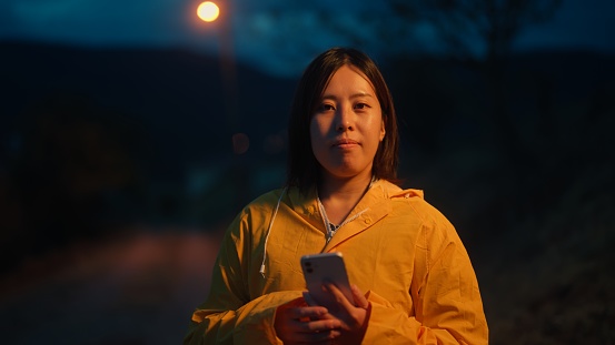A portrait of a female Asian traveler using her mobile smart phone in nature at night.
