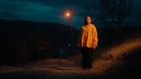 A full length portrait of a female Asian woman in yellow raincoat in nature at night.