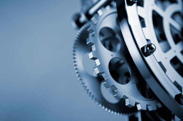 Clockwork Gears and Cogs A blue tinted close up abstract image of gearwheels and cogs in part of a clockwork machine mechanism. The machine is against a plain background. Show with a selective focus with focus on the foreground. With copyspace.  clockworks photos stock pictures, royalty-free photos & images