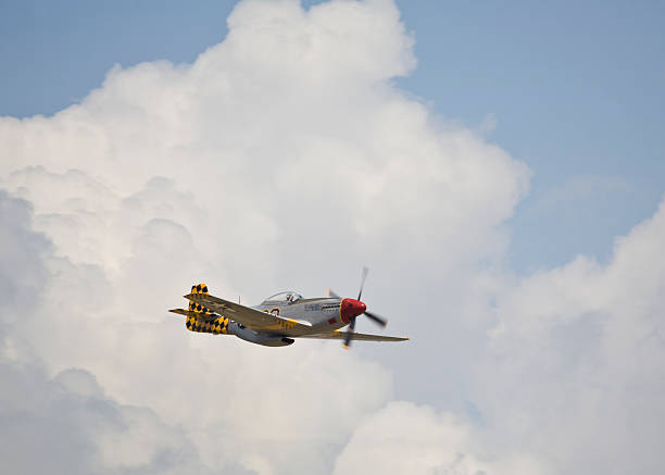 World War II P-51 Mustang Fighter in the Clouds A World War II era P-51 Mustang flying past large clouds. p51 mustang stock pictures, royalty-free photos & images