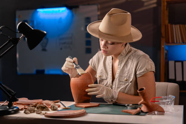 istock Archeologist working late night in office with brush and old vase. 1727909059