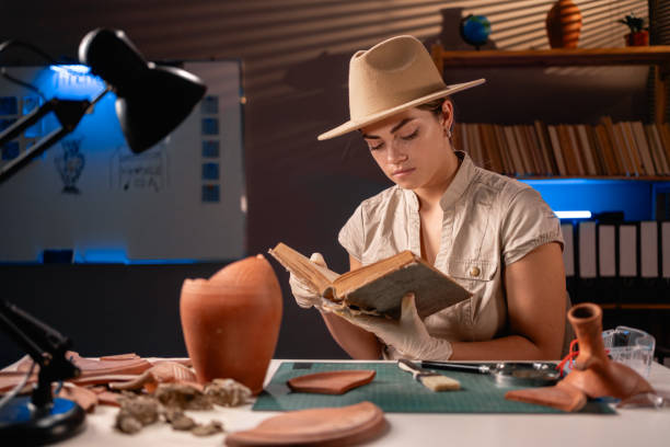 istock Archeologist working late night in office reading old book about archaeology 1727909063
