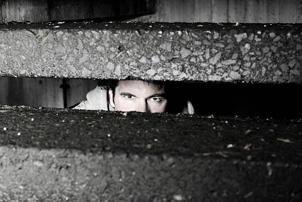 Woman peeking out through window blinds, looking fearful.