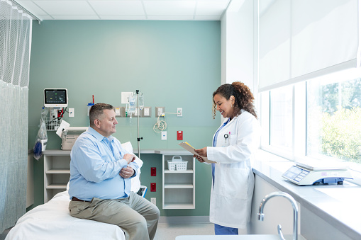 While visiting her patient, the female physician reads over his medical history.