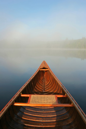 A cedar-strip canoe glides through the calm morning water as mist rises from the lake.