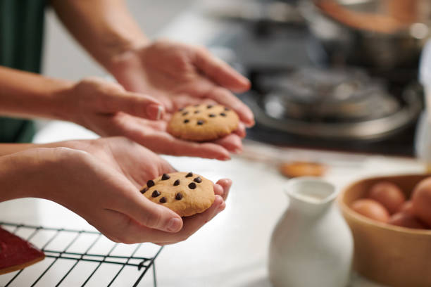 Hands of mother and daughter holding freshly baked cookies with chocolate chips