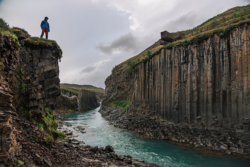 A discoverer is exploring the untouched nature in Iceland. A man is standing on a cliff in nature and watching the canyon river from the top.