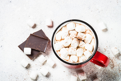 Hot chocolate with marshmallow in red mug at white table. Top view with copy space.