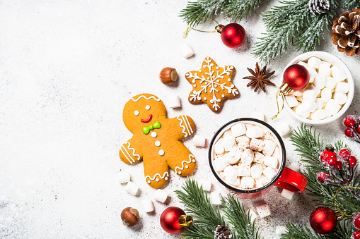 Christmas food. Hot chocolate with marshmallow and gingerbread cookies with holiday decorations at white table. Top view with copy space.