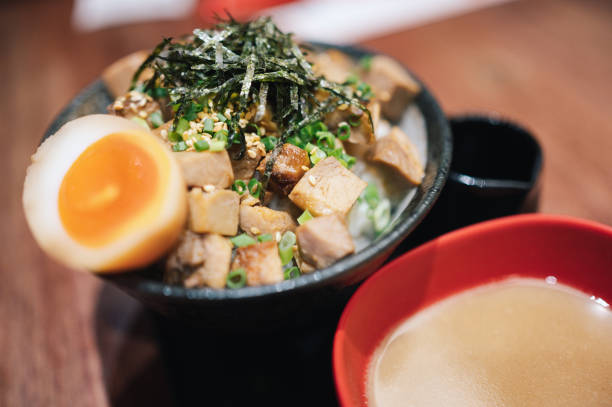 Young Genration alpha women sharing take photo japanese sauce to grilled Pork rice bowl with egg on wooden table in a Japanese restaurant.
