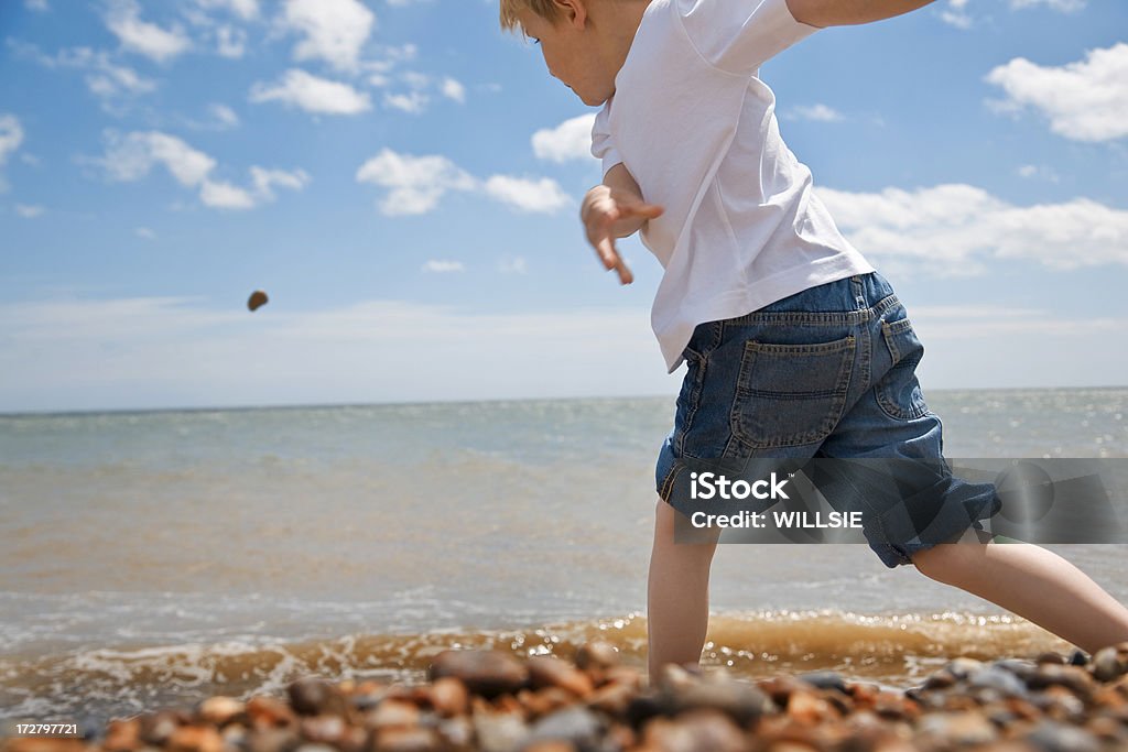 fun at the beach on a glorious day action image of a young boy skimming stones into the sea on a beautiful summer's day. Active Lifestyle Stock Photo