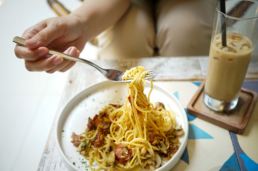 Woman hands holding fork to eat spicy aglio e olio pasta on white plate, served in the cafe, spaghetti aglio e olio with fresh chili or red peper, spaghetty cooked with olive oil, spaghetti aglio e olio with fresh chili or red peper, spaghetty cooked with olive oil