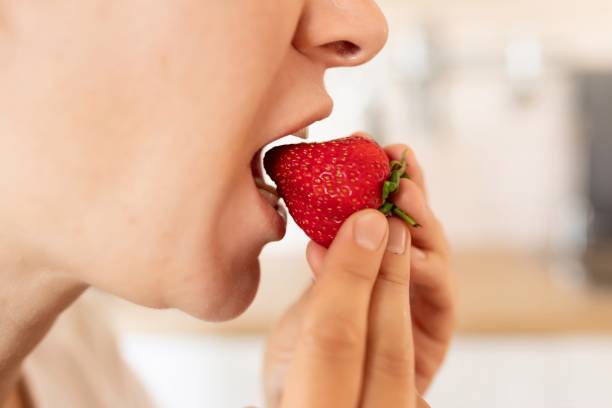 istock woman puts strawberry in mouth while snacking 1727986431