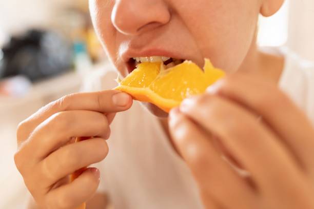 istock Young woman feels hungry and eats orange at breakfast 1727993309
