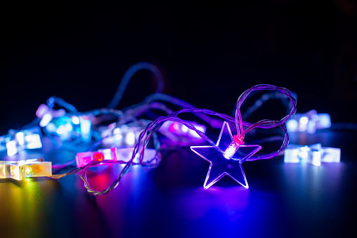 Close up of pink and purple electric christmas string lights garland in the shape of stars, modern holiday home decor on black background