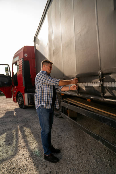 istock Truck driver securing his cargo, checking trailer, tightens tarpaulin 1727998286