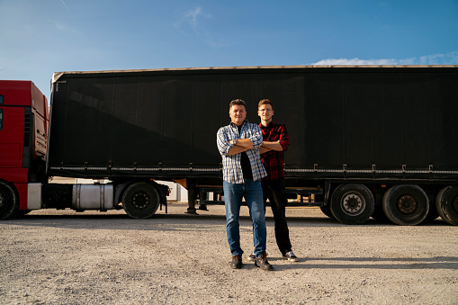 Father and son together starting trucking business, standing proudly in front of long hail truck with trailer
