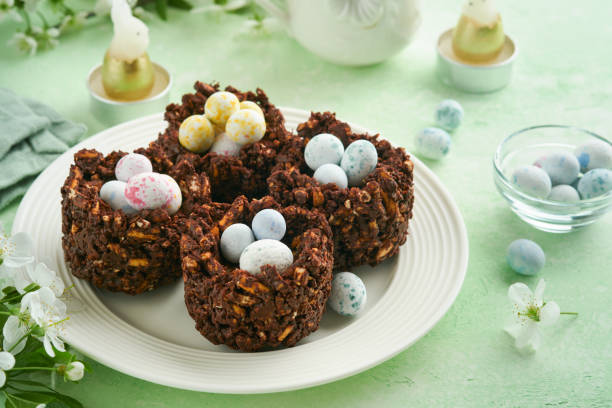 istock Easter chocolate nest cake with mini chocolate candy eggs with blossoming cherry or apple flowers on green background table. Creative recipe for Easter table with holiday decorations. Top view. 1727999976