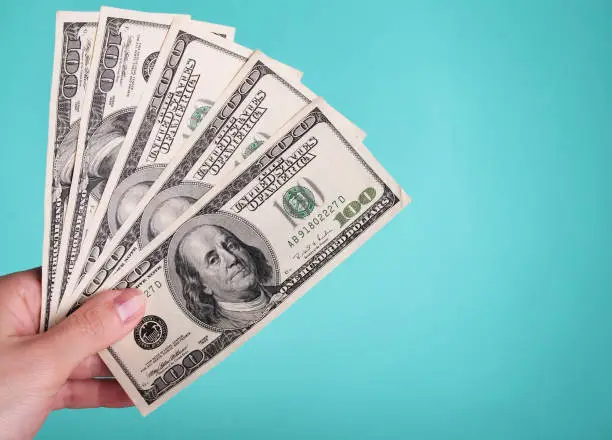 Woman holding 500 dollars against a blue background.