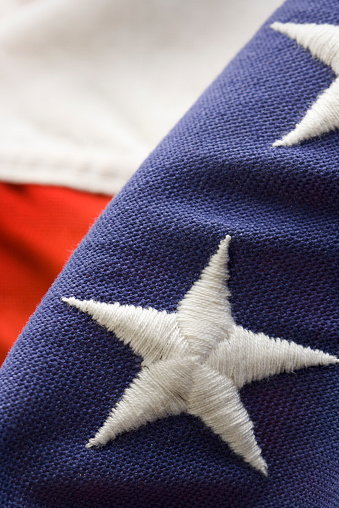 American flag, the United States of America banner in close-up featuring one embroidered, sewn star, weathered thread stitching and faded red, white, and blue fabric details. Called Old Glory or Stars and Stripes, this patriotic banner decorates Fourth of July (Independence Day), Memorial Day, Veterans Day, and other national holidays. 
