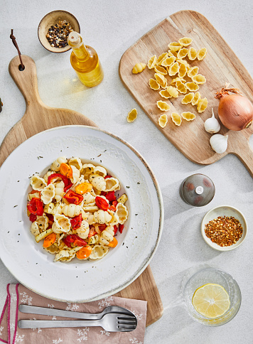 Healthy vegetarian pasta, made of zucchini, red pepper, carrot and garlic, served on an elegant ceramic plate, with fresh vegetables and herbs around, olive oil and pepper, on a white granite ceramic natural kitchen or restaurant table, representing a wellbeing and a healthy lifestyle, food indulgence, top view image with a copy space
