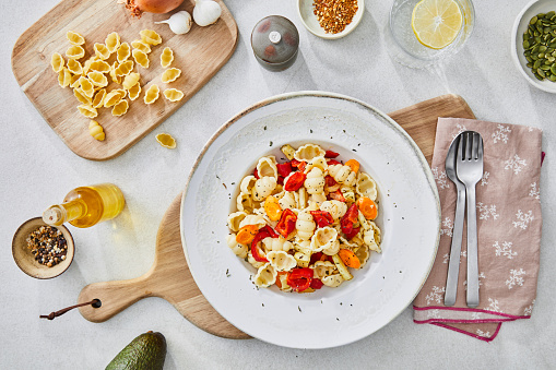 Healthy vegetarian pasta, made of zucchini, red pepper, carrot and garlic, served on an elegant ceramic plate, with fresh vegetables and herbs around, olive oil and pepper, on a white granite ceramic natural kitchen or restaurant table, representing a wellbeing and a healthy lifestyle, food indulgence, top view image with a copy space