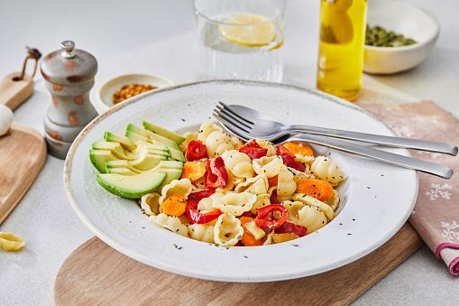 Healthy vegetarian pasta, made of zucchini, red pepper, carrot and garlic, served on an elegant ceramic plate, with fresh vegetables and herbs around, olive oil and pepper, on a white granite ceramic natural kitchen or restaurant table, representing a wellbeing and a healthy lifestyle, food indulgence, an image with a copy space