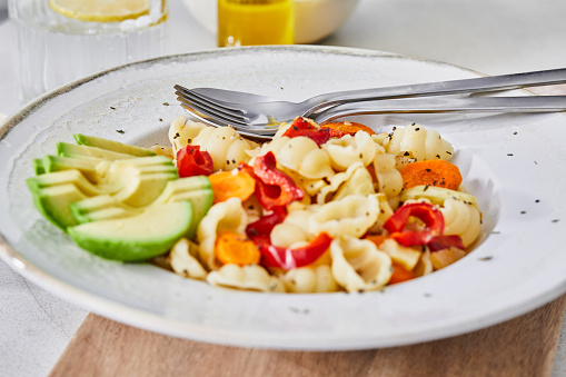 Healthy vegetarian pasta, made of zucchini, red pepper, carrot and garlic, served on an elegant ceramic plate, with fresh vegetables and herbs around, olive oil and pepper, on a white granite ceramic natural kitchen or restaurant table, representing a wellbeing and a healthy lifestyle, food indulgence, an image with a copy space