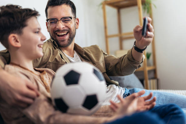 istock Father and son watching a soccer game while eating popcorn. 1728005996