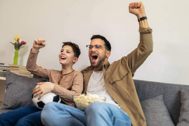 istock Father and son watching a soccer game while eating popcorn. 1728006682