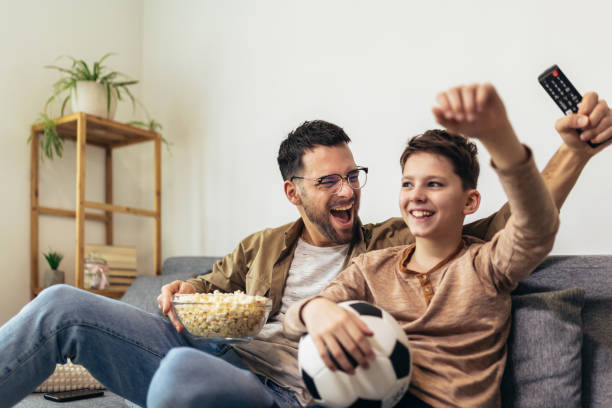 istock Father and son watching a soccer game while eating popcorn. 1728006991