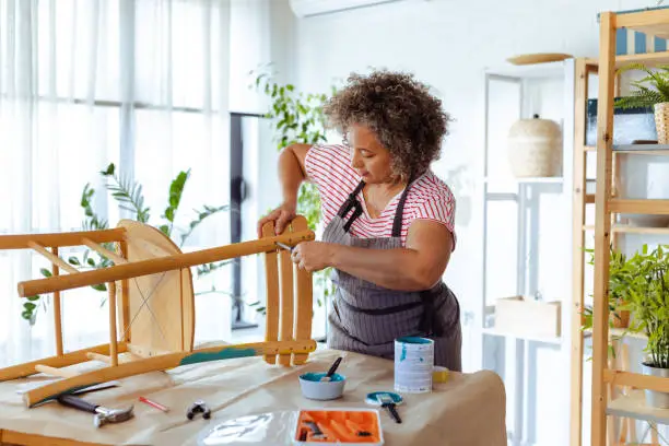 Mature woman wearing an apron and repairing old furniture at home. DIY concept