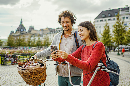 Young couple looking at a mobile phone while standing beside their bicycles through the city