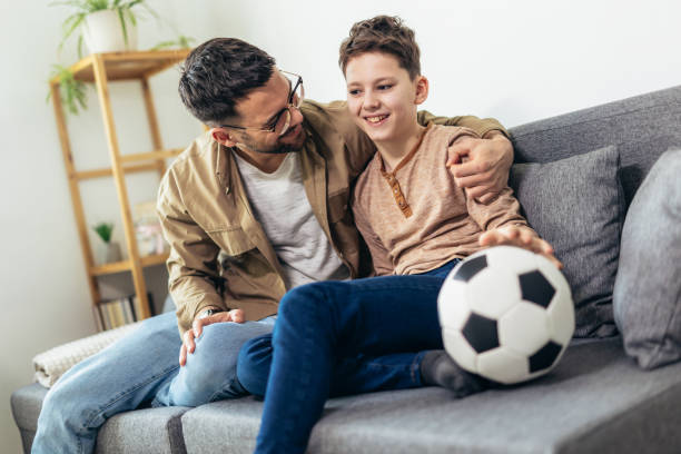 istock Father and son watching a soccer game while eating popcorn. 1728012054
