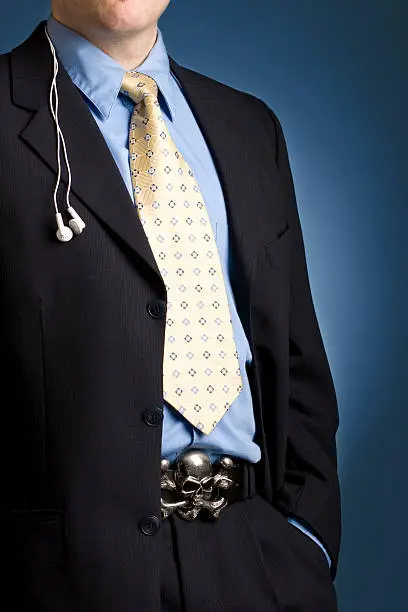 Confidant young businessman wearing white headphones and  skull belt buckle with suit.See more images from this series: