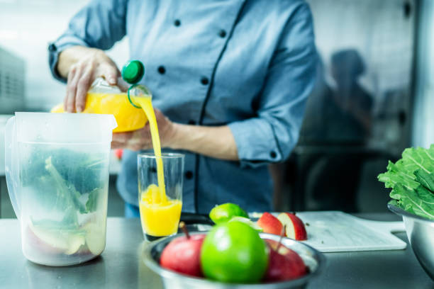 Chef pouring orange juice into a drinking glass at commercial kitchen
