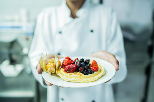 Close-up of a chef holding waffle with fruit at commercial kitchen