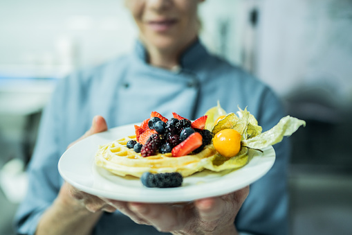 Close-up of a chef holding waffle with fruit at commercial kitchen