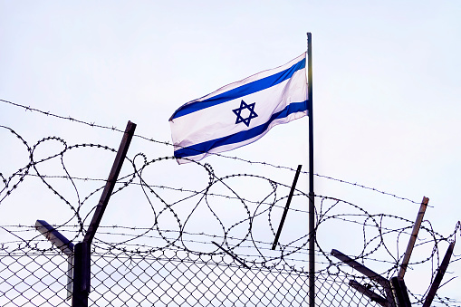 View of israeli flag behind barbed wire against cloudy sky. border post on the border of israel. The checkpoint at the embassy of the country. the Palestinian-Israeli border.