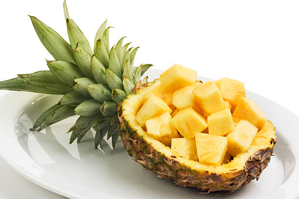 Cubed yellow pineapple in its own halved bowl and setting on a platter. A tropical climate fruit, it is fresh chopped and presented as a prepared sweet food. Pineapple is a readily available grocery.