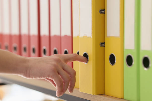 Hand of secretary taking yellow ring binder with documents. Organized structure of colorful folders with archive files put in row on shelf
